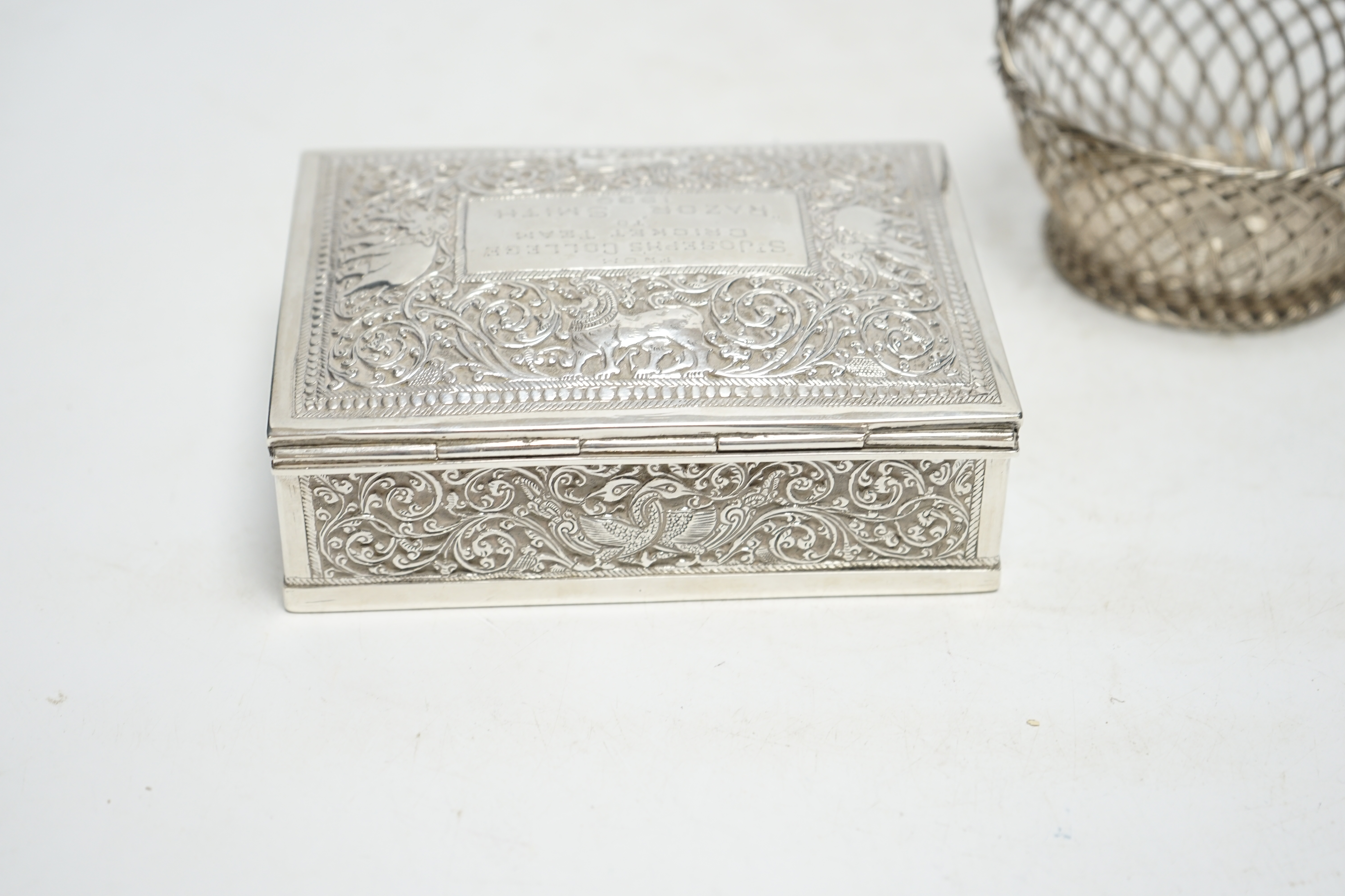 An Indian white metal mounted rectangular cigarette box, with engraved inscription, 'From St. Joseph's College Cricket Team, to 'Razor' Smith, 1930', 12.9cm, together with a white metal open work basket. Condition - fair